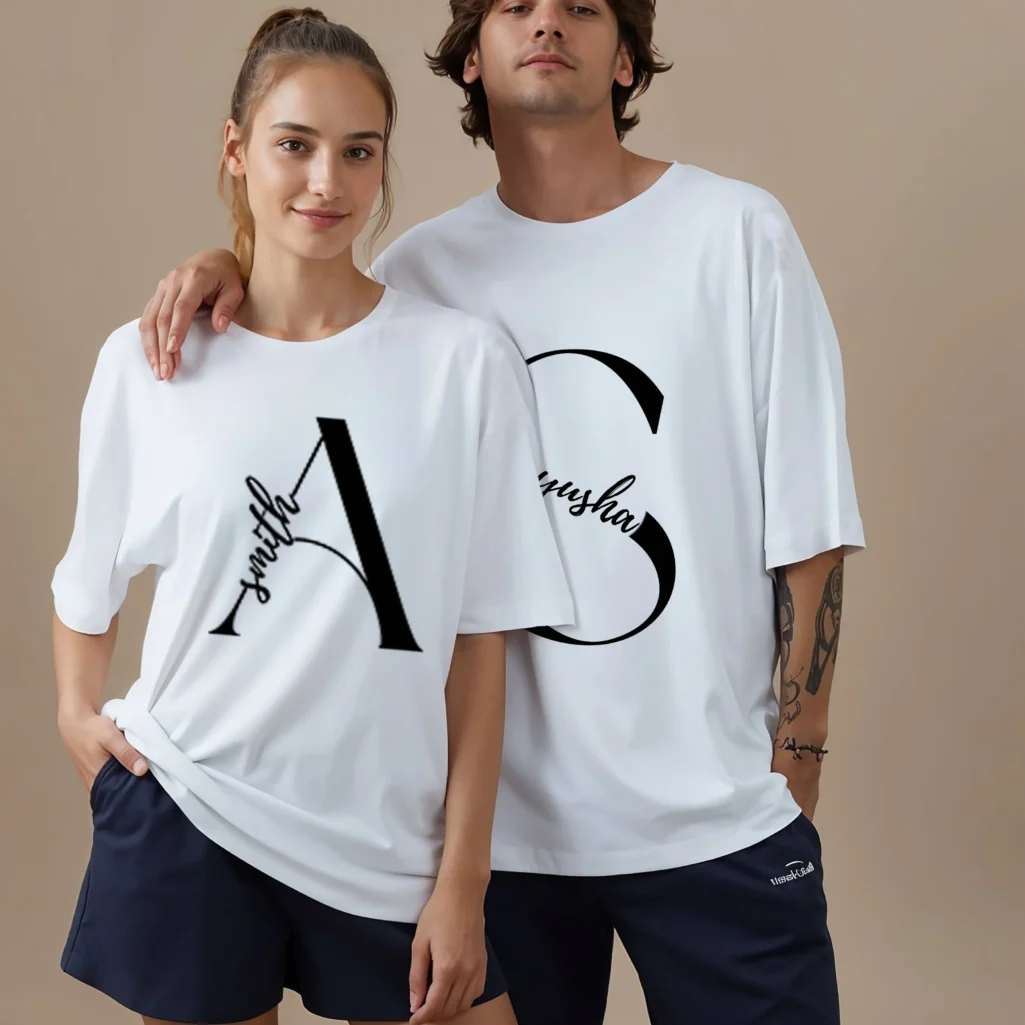 Couple wearing personalized white oversized matching t-shirts with custom names printed on premium cotton fabric for pre-wedding photoshoots and anniversary gifting.
